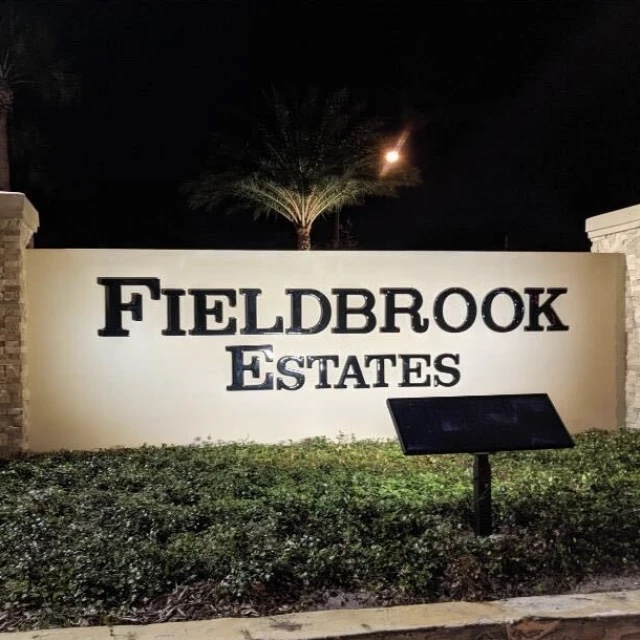 Community entrance sign lit at night by a ground-mounted solar sign light